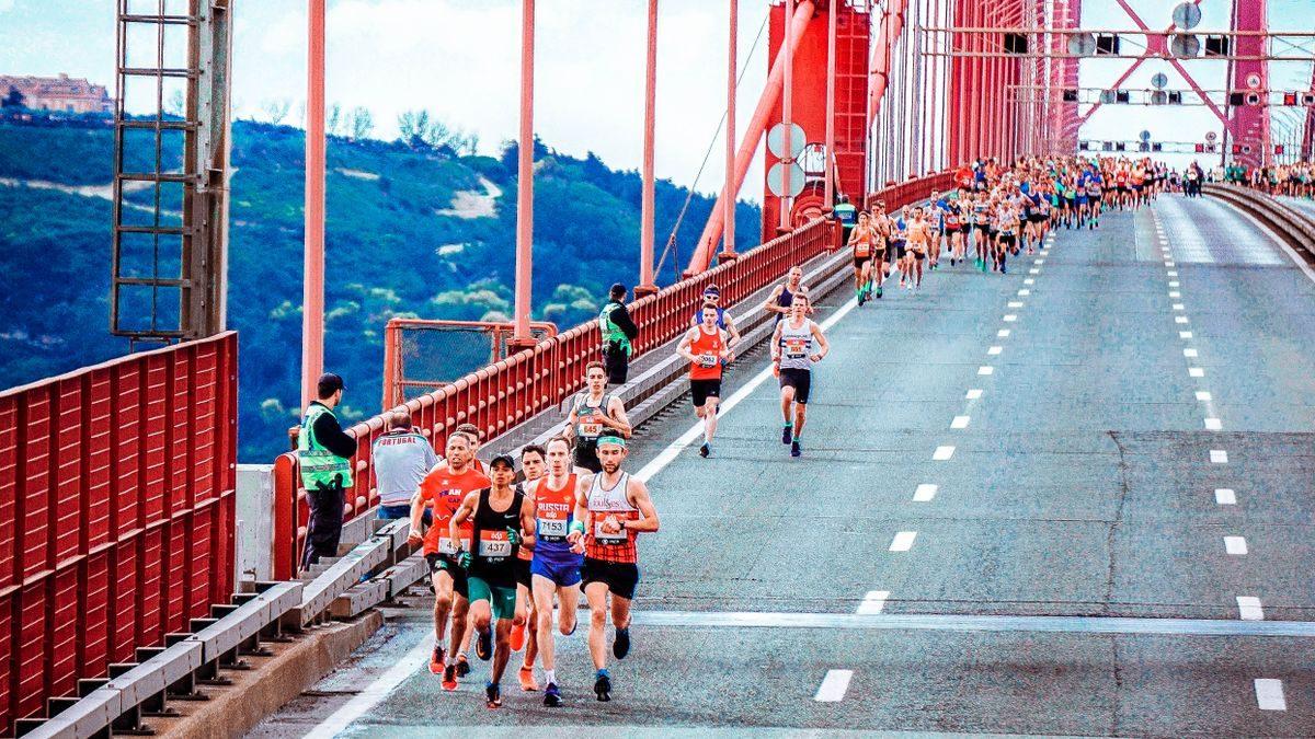 Runners crossing a red suspension bridge during a road race.